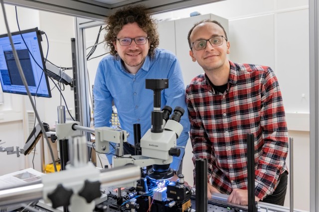Two researchers standing behind a microscope in a laboratory.